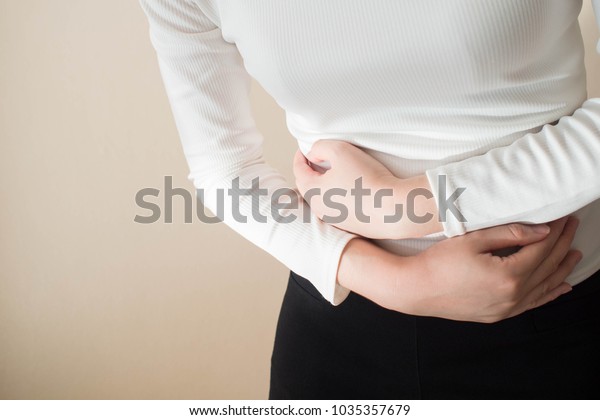 Young female suffering form stomach ache on gray
background w/ copy space. Causes of abdominal pain include
menstruation pain, gastritis, stomach ulcer, food poisoning,
diarrhea or IBS. Close
up.