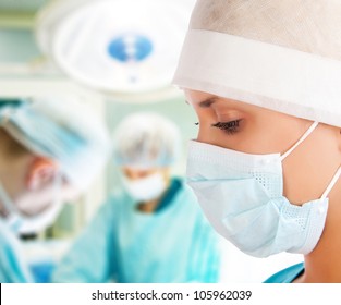 Young Female Surgeon With Two Doctors On Background In Operation Room