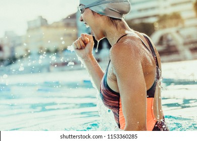 Young female swimmer celebrating victory in the swimming pool. Excited woman swimmer with clenched fist inside the swimming pool.