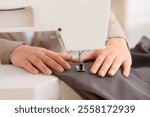 Young female tailor using sewing machine for brown fabric near table in atelier, closeup