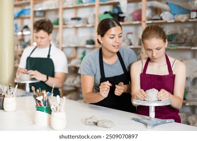 Young female teacher in apron helps teenager boy and teenager girl students to make product from clay in ceramic workshop - Powered by Shutterstock