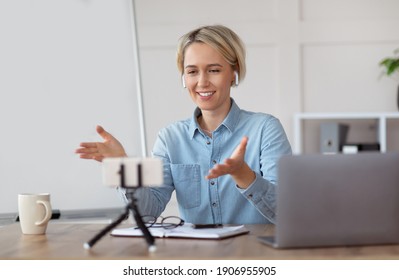 Young Female Teacher Conducting Online Lesson Near Blank Blackboard, Using Cellphone And Laptop For Distance Education, Copy Space. Millennial Tutor Chatting With Students On Webcam