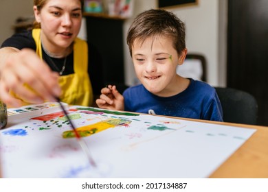 Young female teacher explain, talk at desk with a down syndrome schoolboy. Color painting for disabled kids, child who are down syndrome and student teacher, development of children with spesial needs - Shutterstock ID 2017134887