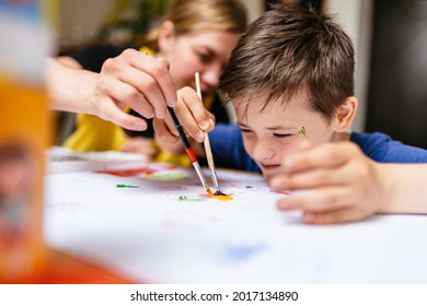 Young female teacher explain, talk at desk with a down syndrome schoolboy. Color painting for disabled kids, child who are down syndrome and student teacher, development of children with spesial needs - Shutterstock ID 2017134890