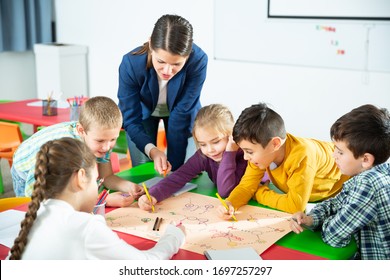 Young female teacher and happy schoolkids playing interesting board game during lesson in classroom - Shutterstock ID 1697257297