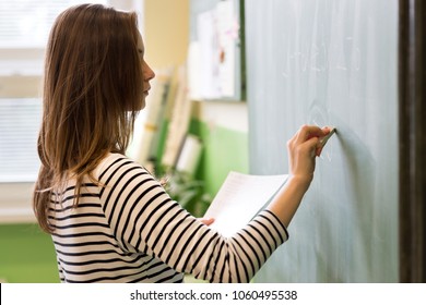 Young female teacher or a student writing math formula on blackboard in classroom.  - Powered by Shutterstock