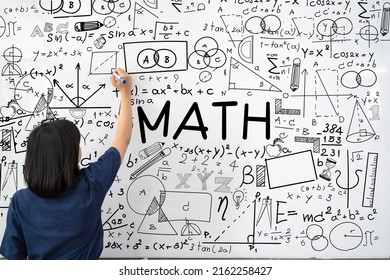 Young female teacher is writing math formulas and equations on whiteboard to explain educational material task to her pupils or students in college or university classroom