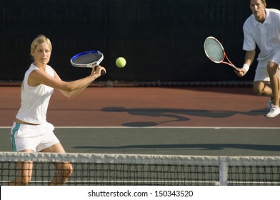 Young female tennis player hitting ball with doubles partner standing in background
