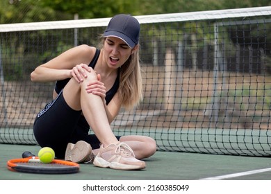 Young female tennis player sitting on court injured knee while playing a match and showing a face of pain - Powered by Shutterstock