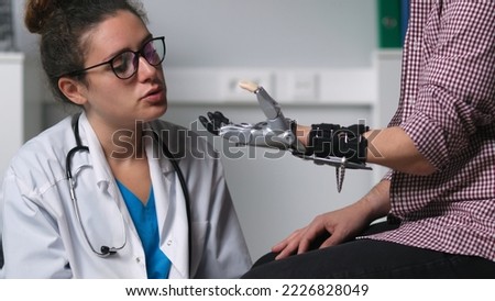 Young female therapist examine patient moving hand prosthesis in hospital. Handicapped man with amputated limb test bionic arm with doctor