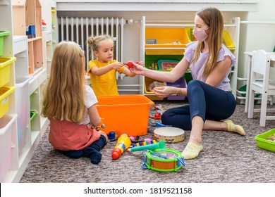 Young Female Therapist Wearing Protective Face Mask Playing With Two Toddler Girls During Occupational Child Therapy.