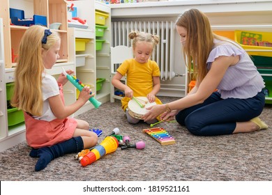 Young Female Therapist Wearing Protective Face Mask Playing With Two Toddler Girls During Occupational Child Therapy.