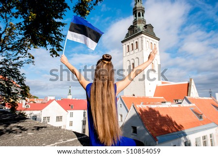 Young female tourist with estonian flag in front of saint Nicholas church in the old town of Tallinn. Woman having great vacations in Estonia