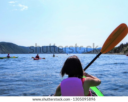 A young female tourist in a kayak exploring the beautiful waters in Bonne Bay with a group of kakayers, in Gros Morne National Park, Newfoundland, Canada.      