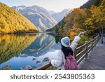 Young female tourist relaxing and enjoying at beautiful autumn scenery landscape at mirror lake in jiuzhaigou national park