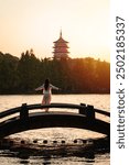 Young female tourist relaxing and looking at beautiful sunset and Chinese pagoda at Xihu lake, Hangzhou