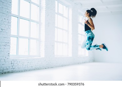 Young female in tracksuit jumping doing aerobics cardio exercises for losing weight and training strength,sportswoman doing leaps burning calories on pilates workout enjoying active lifestyle