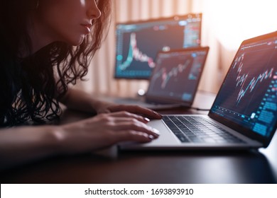 Young Female Trader With Laptop And Screen Looking At Stock Charts