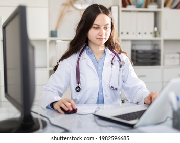 Young Female Trainee Doctor Who Is Undergoing An Internship At A Medical Clinic Is Sitting At Workplace At A Computer