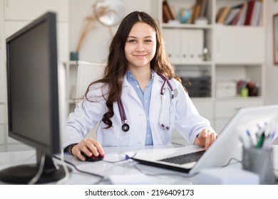 Young Female Trainee Doctor Who Is Undergoing An Internship At A Medical Clinic Is Sitting At Workplace At A Computer