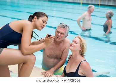 Young female trainer showing time to senior swimmers at poolside - Powered by Shutterstock