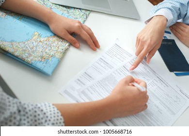Young female travel agent consultant in tour agency with a customer signing documents