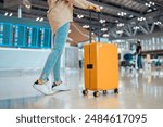 Young female traveler passenger walking with a yellow suitcase at the modern Airport Terminal, Back view of woman on her way to flight boarding gate, Ready for travel or vacation journey