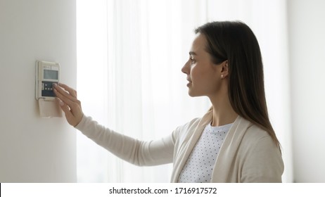 Young female turn on switch smart home wall control panel, millennial woman regulate temperature use air condition device modern automatic AC indoors, girl use house security system or fire alarm - Shutterstock ID 1716917572
