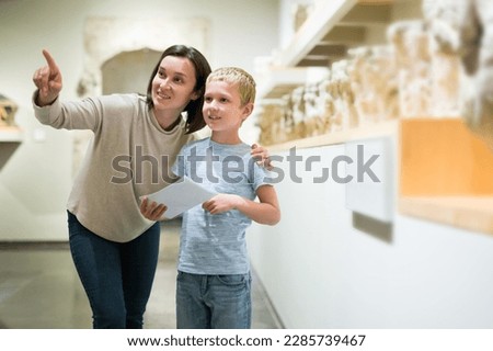 Young female tutor with boy looking at exposition in museum of ancient sculpture, pointing to something