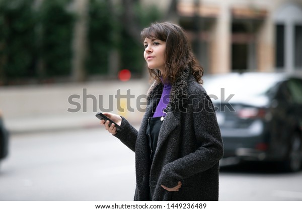 Young female using\
mobile phone app and waiting for a rideshare or pedestrian tourist\
checking online map for gps navigation.  Depicts city life and how\
millennials travel.