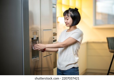 Young Female Using The Refrigerator Water Dispenser