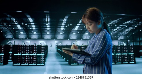 A Young Female Using Tablet While Working in Server Room in Contemporary Data Center. IT Technician. Cloud Storage Technology, Database, Engineering. High quality photo