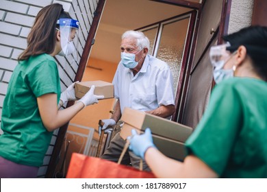 Junge Freiwillige in Maske gibt einem älteren Mann Kisten mit Essen in der Nähe seines Hauses. isoliert. Coronavirus covid-19. Spende