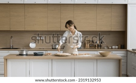 Young female wear apron cooking pizza, sprinkle dish with cheese, enjoy cooking in modern cozy kitchen, prepare Italian cuisine from natural ingredients on weekend at home, homemade cookery, chores