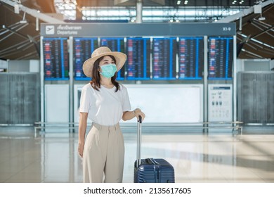 Young female wearing face mask with luggage walking in airport, protection Coronavirus disease infection, Asian woman traveler with hat. Time to travel, Test and Go and vaccine booster dose concept