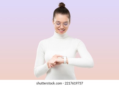 Young female in white sweater   glasses looking at smartwatch her wrist  checking time  glad she is not late  isolated purple gradient background