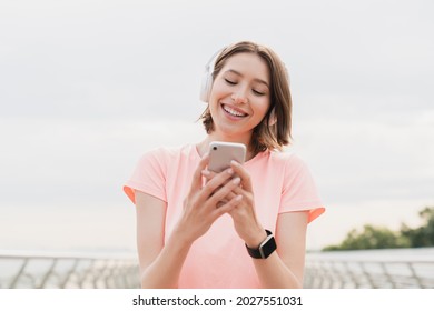 Young female woman student walking in the city listening to the music in headphones earphones using smart phone for musical application, searching for favorite soundtrack singer song outdoors. - Powered by Shutterstock