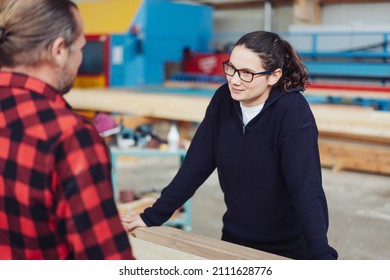 Young Female Woodworker Listening To A Male Colleague With A Smile In An Industrial Woodworking Factory