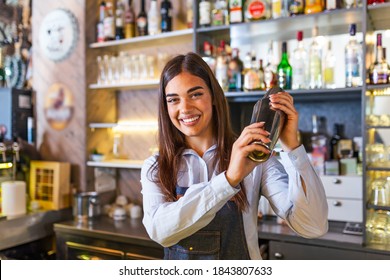 Young Female Worker At Bartender Desk In Restaurant Bar Preparing Coctail With Shaker. Beautiful Young Woman Behind Bar Making Coctail