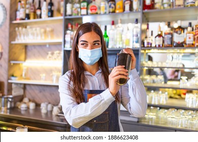 Young Female Worker At Bartender Desk In Restaurant Bar Preparing Coctail With Shaker. Beautiful Young Woman Behind Bar Wearing Protective Face Mask