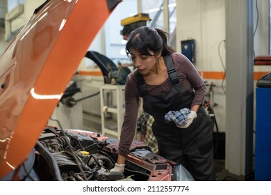 Young female worker of car maintenance service repairing vehicle while bending over open hood with broken engine
