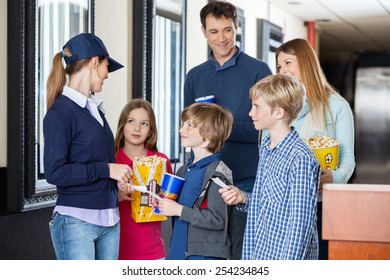 Young Female Worker Checking Movie Tickets Of Family At Cinema