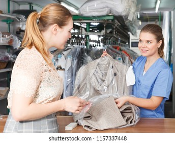 Young Female Worker Of Dry Cleaner Returning Clean Clothes To Customer On Reception