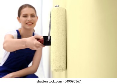 Young Female Worker Painting Wall In Room