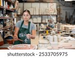 Young female worker in pottery factory lowers fired clay plates and cups into a container with glaze