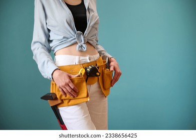 Young female worker with tool belt holding an instrument in hands isolated on background. Pretty caucasian female with tools planning new project. Portrait in studio. Crop view. - Powered by Shutterstock