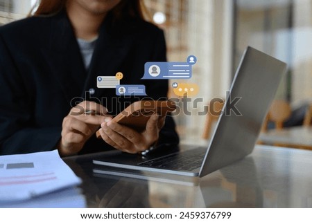 Young female worker using mobile phone with notification icons commenting in online community