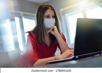 Young female worker  wearing a protective mask while she is  at home and attending at a  meeting on her computer during the lockdown due to the coronavirus