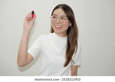 Young female  writing something on glass board with a marker. Selective focus. woman writing something on glass board with marker on blur background of light office. - Powered by Shutterstock