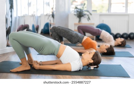 Young female yoga instructor guiding group of women through various asanas and transitions during yoga practice session in modern studio .. - Powered by Shutterstock